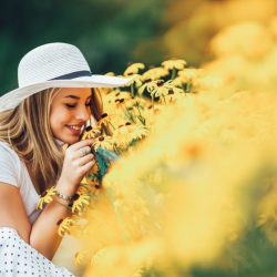 Junge Frau mit Hut riecht an einer Blume